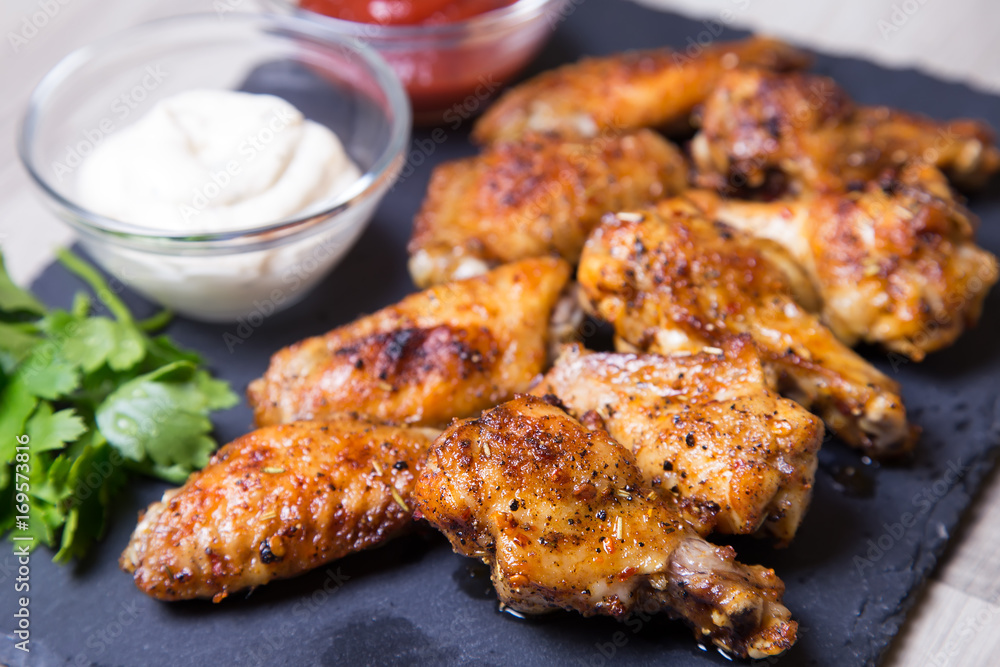 Chicken wings of a barbecue with two sauces on a black board. Close-up. Selective focus. Chicken wings of a barbecue with two sauces on a black board. Close-up. Selective focus.