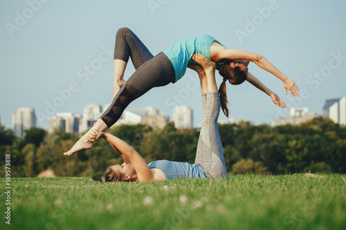 Two young beautiful Caucasian women yogi doing high flying whale acro yoga pose. Women doing stretching workout in park outdoors at sunset. Healthy lifestyle modern activity photo