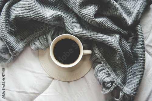 Cozy winter home background, cup of hot coffee with marshmallow, warm knitted sweater on white bed background, vintage tone. Lifestyle concept