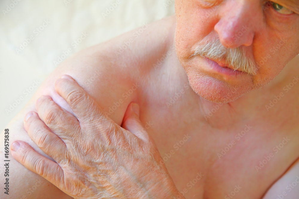 Naklejka premium An older man with a hand on an aching shoulder joint