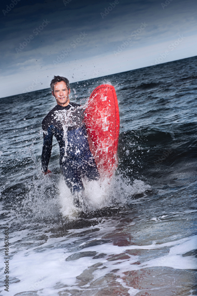 man coming out of the water with his surfboard under his arm Stock