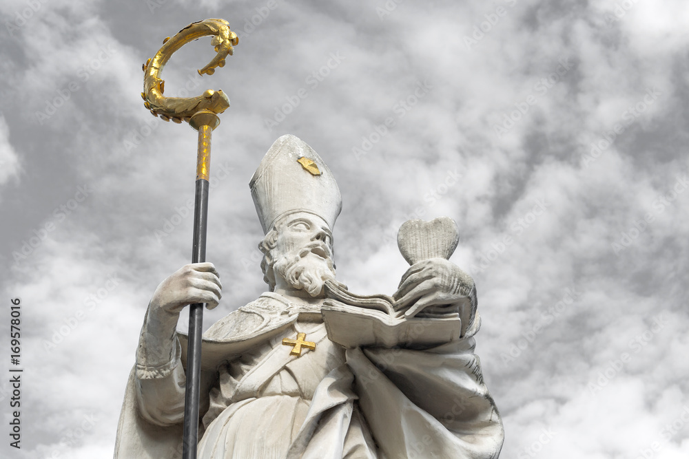 White marble sculpture of Saint Augustine with golden cross and bishop's crook, holding a heart in his left hand - obrazy, fototapety, plakaty 