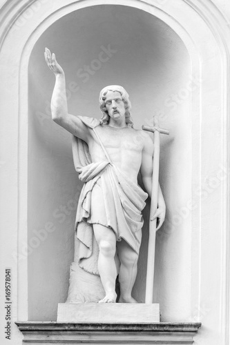 White marble sculpture of holy man with a cross and uplifted hand