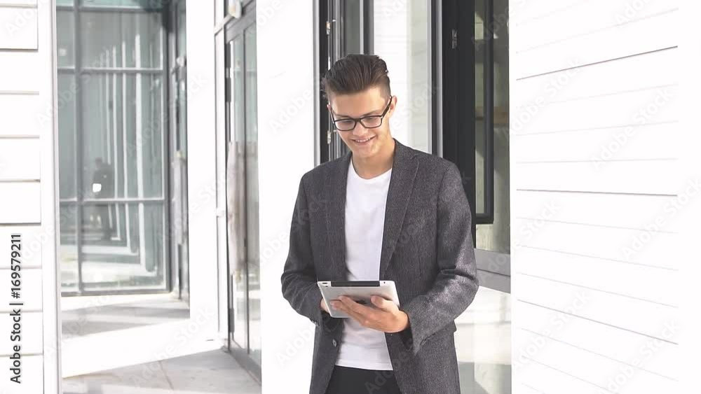Young businessman uses tablet on background of modern building. Young businessman uses tablet on background of modern building.