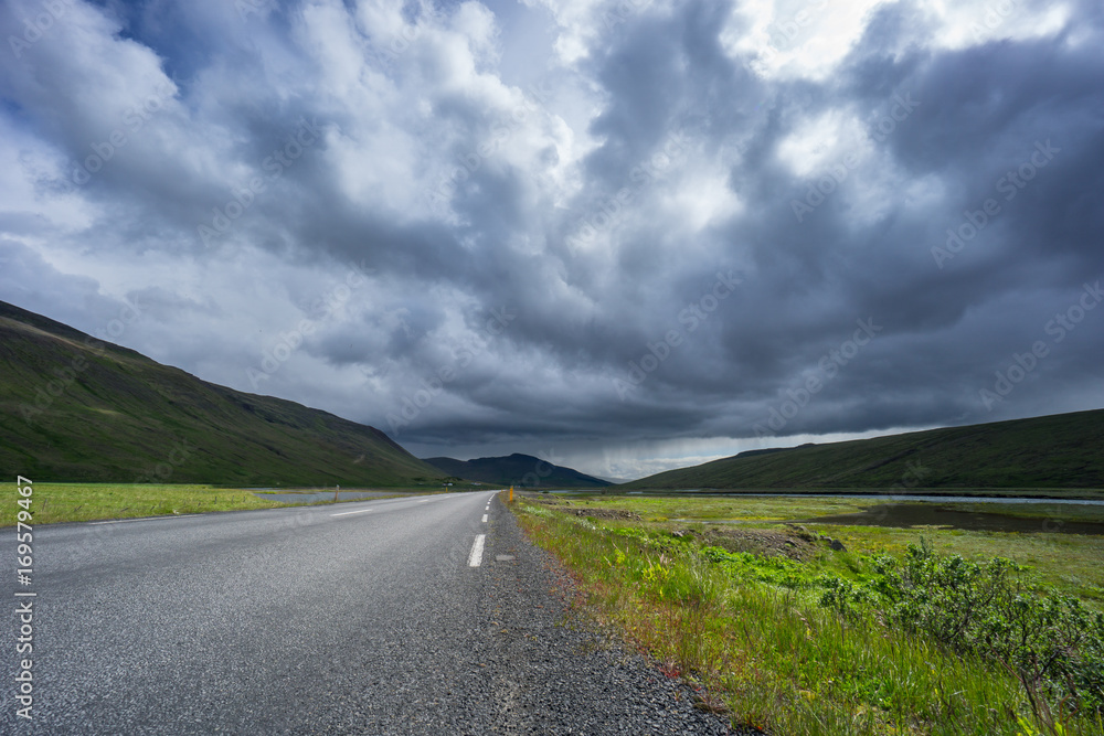 Iceland - Road through green valley and river with rain far away