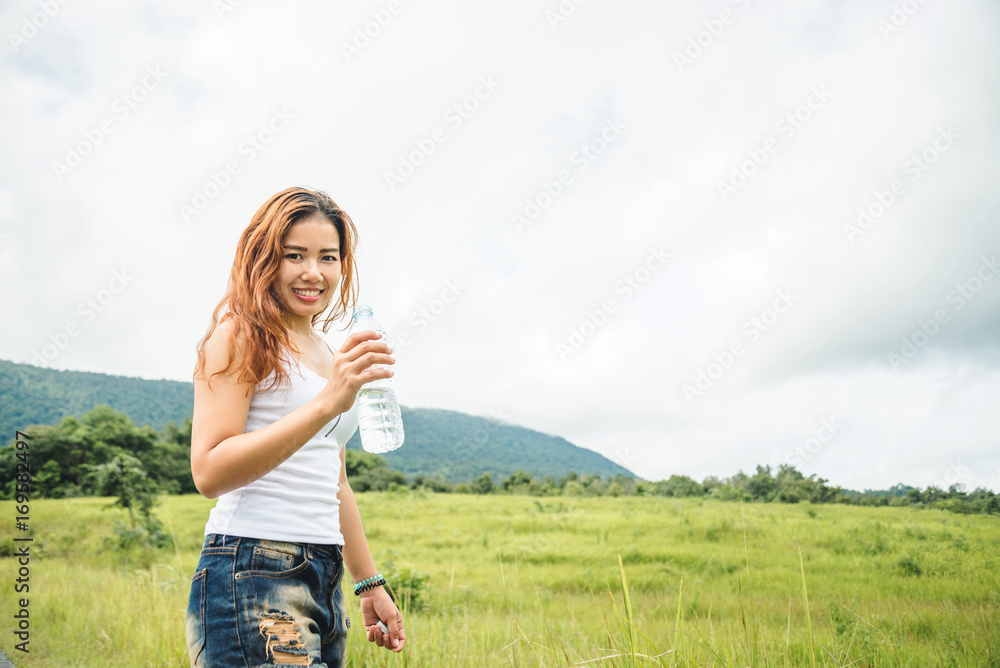 Asian women travel relax in the holiday. Drink Water on a green pasture.