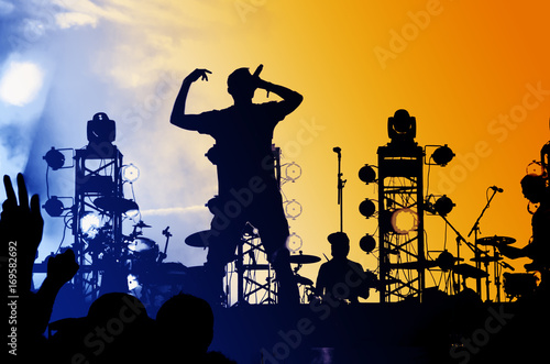 The vocalist is a rock star with a microphone on the big stage in front of a crowd of fans.