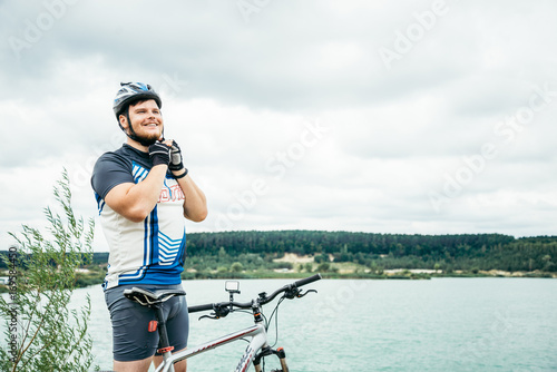 man near standing near lake with bicycle and check helmet