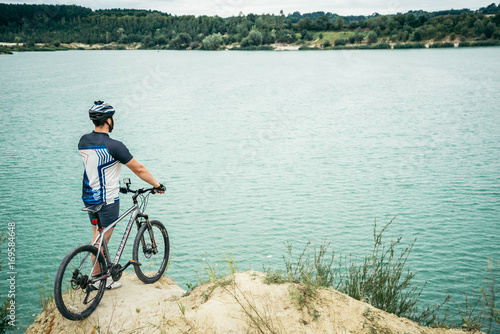 man with bicycle stand on the hill and looking at the lake