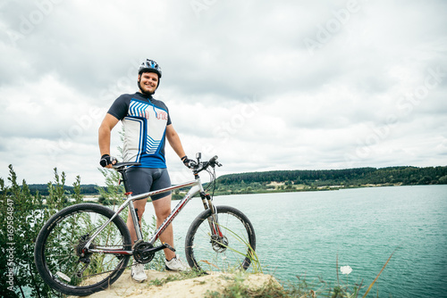 man with bicycle stand on the hill and looking at the lake