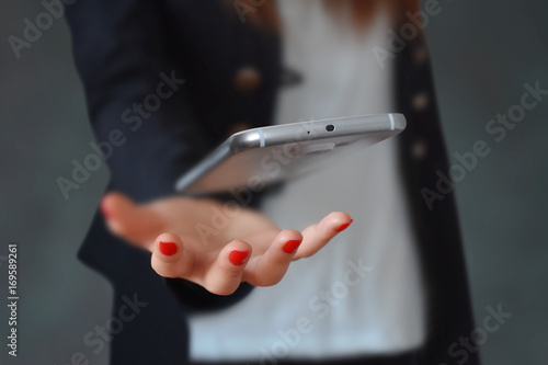 Modern white smartphone floating above business woman hand. Business technology concept