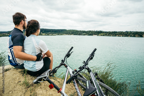 couple sits and looking at the lake two bicycles near them