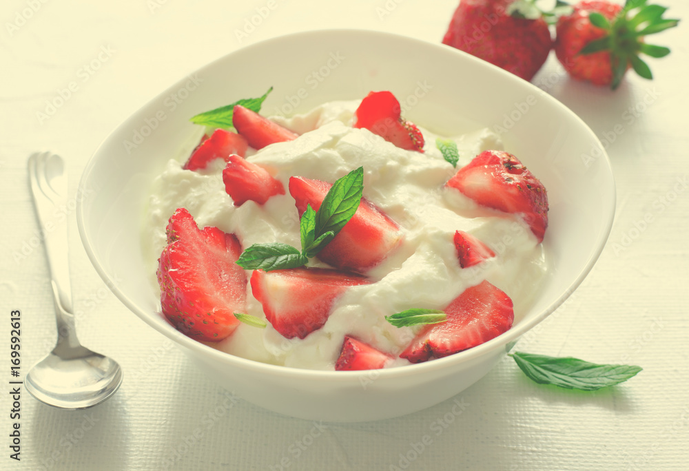 Breakfast with bowl of thick organic greek yogurt and fresh strawberries on white backgfound. Toned
