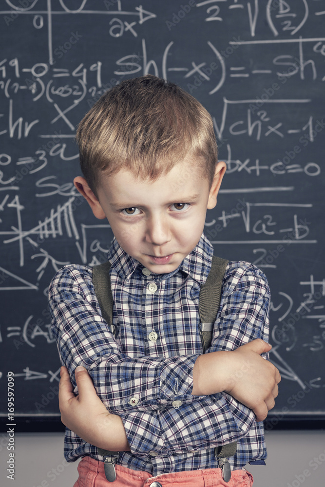 child arms crossed contrite expression. blackboard in the background. school, will,disappointment