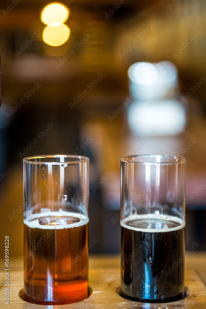 Two small glasses of beer for tasting in rustic room with pale ale and dark stout Two small glasses of beer for tasting in rustic room with pale ale and dark stout