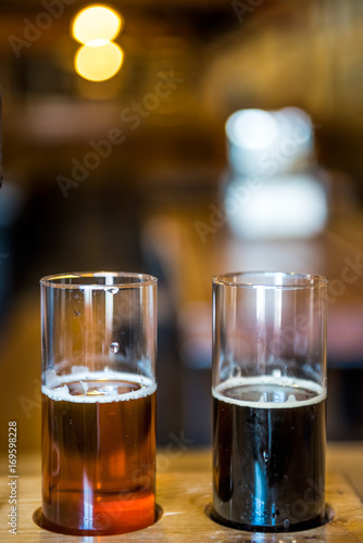 Two small glasses of beer for tasting in rustic room with pale ale and dark stout
