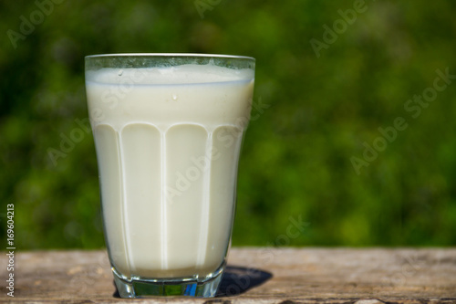Glass of milk on wooden table with nature background