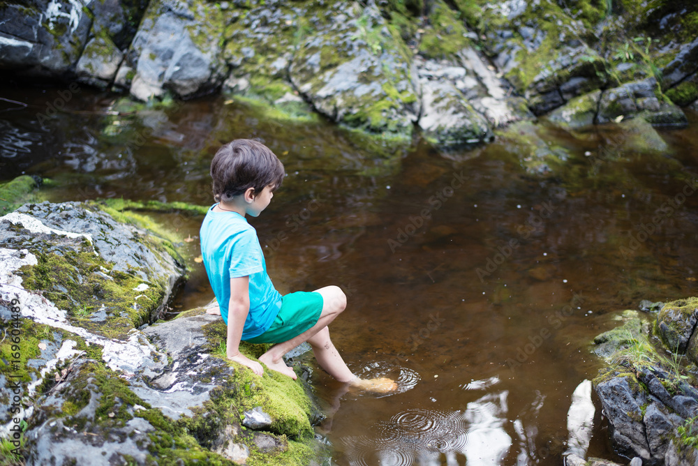 the boy is standing on the bank of a stream the boy is standing on the bank of a stream