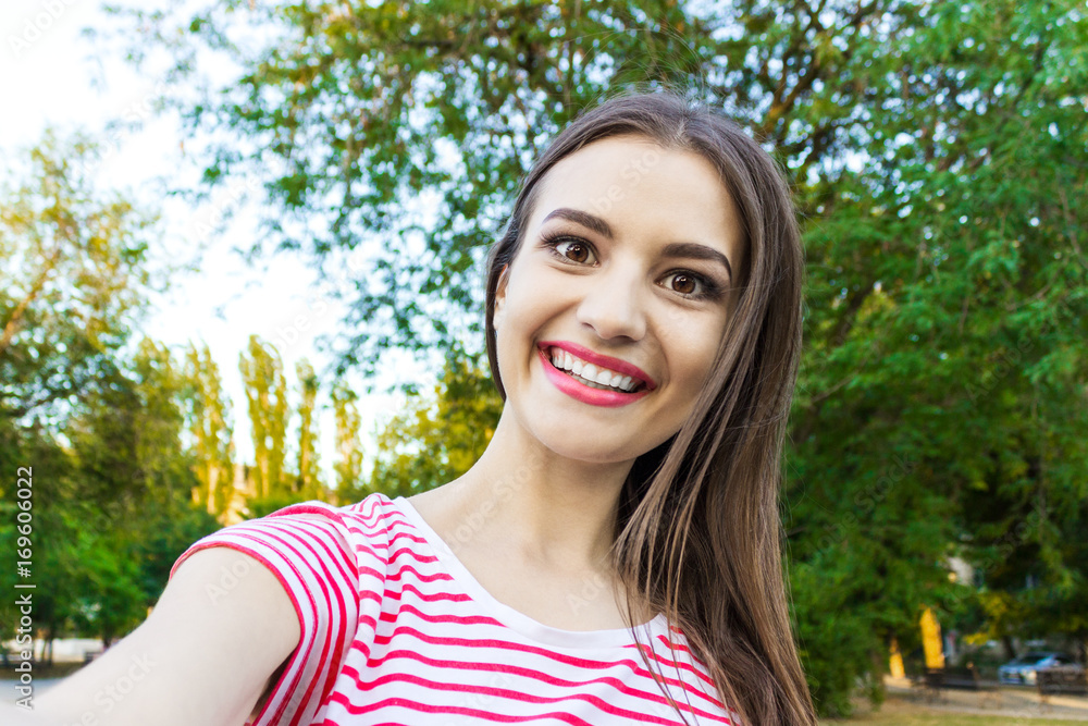 Pretty smiling girl making selfie, long-haired brunette in white clothes, closeup Pretty smiling girl making selfie, long-haired brunette in white clothes, closeup