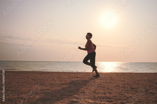 senior woman jogging on sea beach at the sunrise