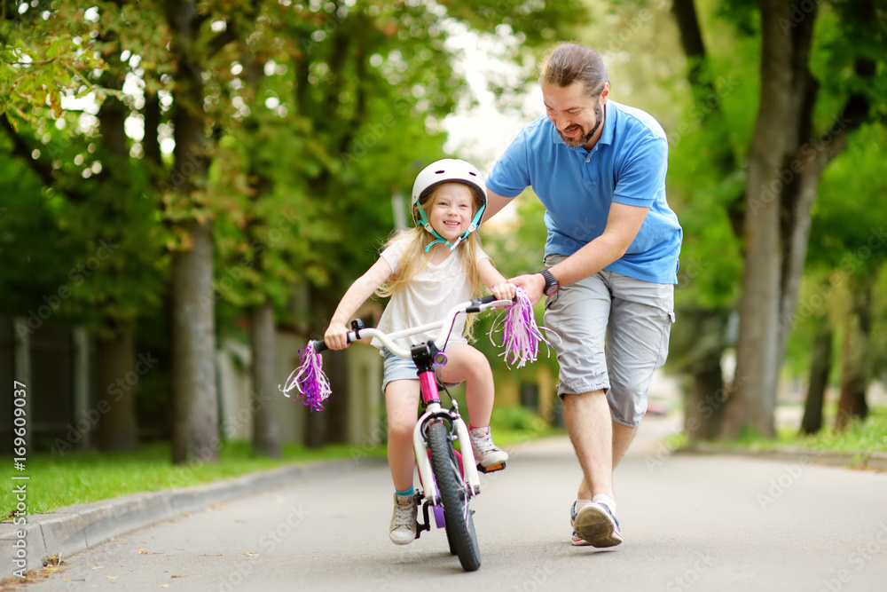 Happy father teaching his little daughter to ride a bicycle. Child learning to ride a bike. Happy father teaching his little daughter to ride a bicycle. Child learning to ride a bike.