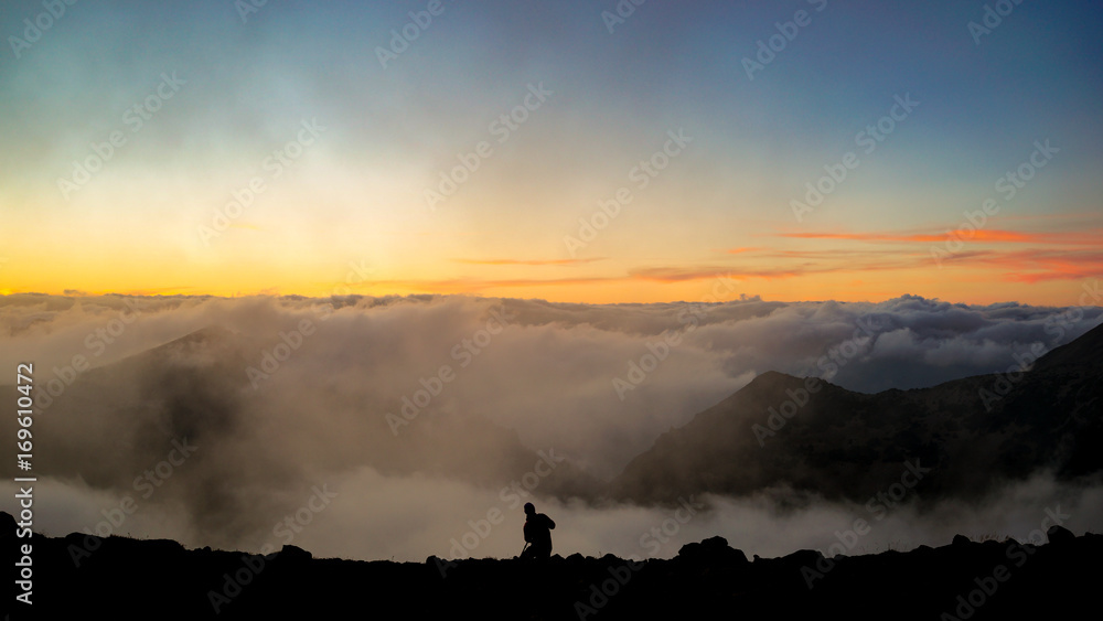 Fototapeta premium The Photographer Taking Pictures on the Mountain with Clouds During Sunset/Sunrise