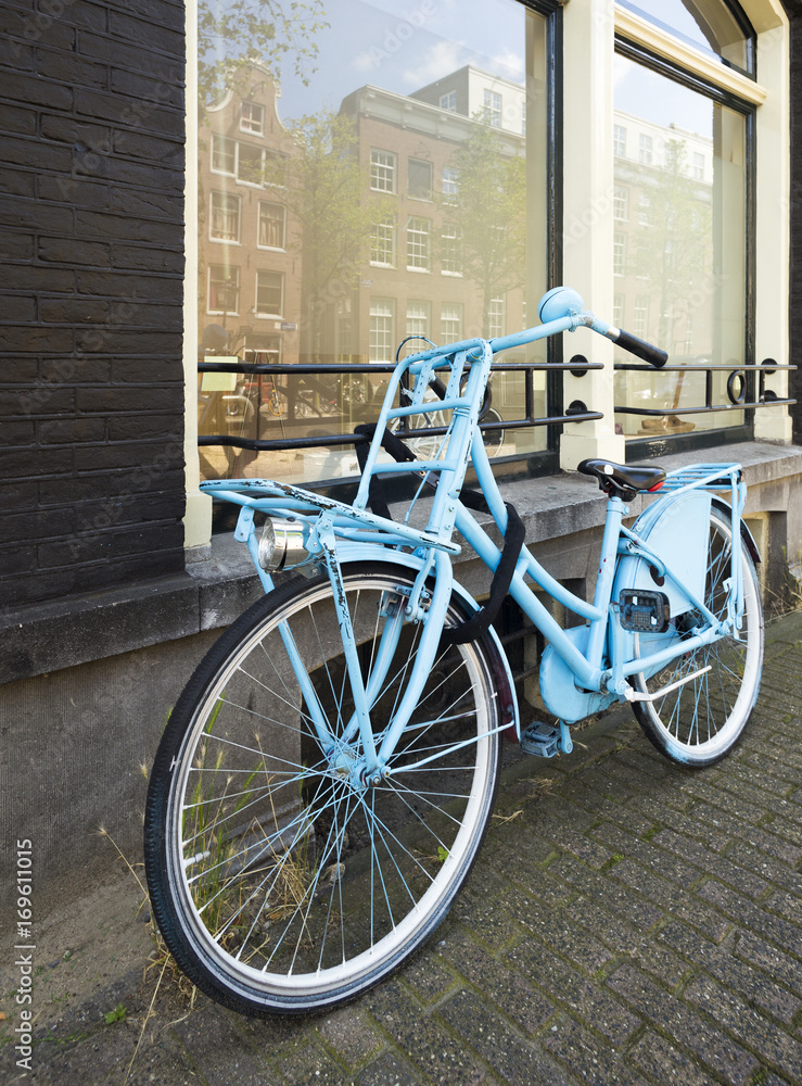 Blue bicycle left at wall with large windows Blue bicycle left at wall with large windows