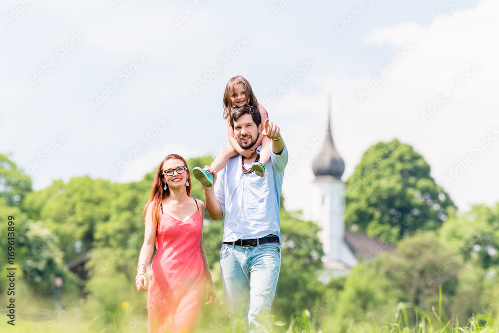 Fototapeta premium Family walking on meadow having walk, dad is carrying his little daughter on the shoulders