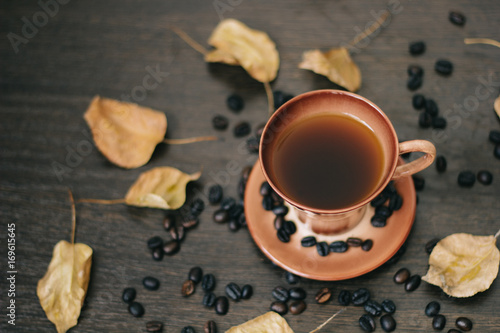 a cup of black coffee in the mug, surrounded by autumn leaves and coffee beans, top view.