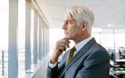 Slika na platnu Thoughtful senior businessman standing by window