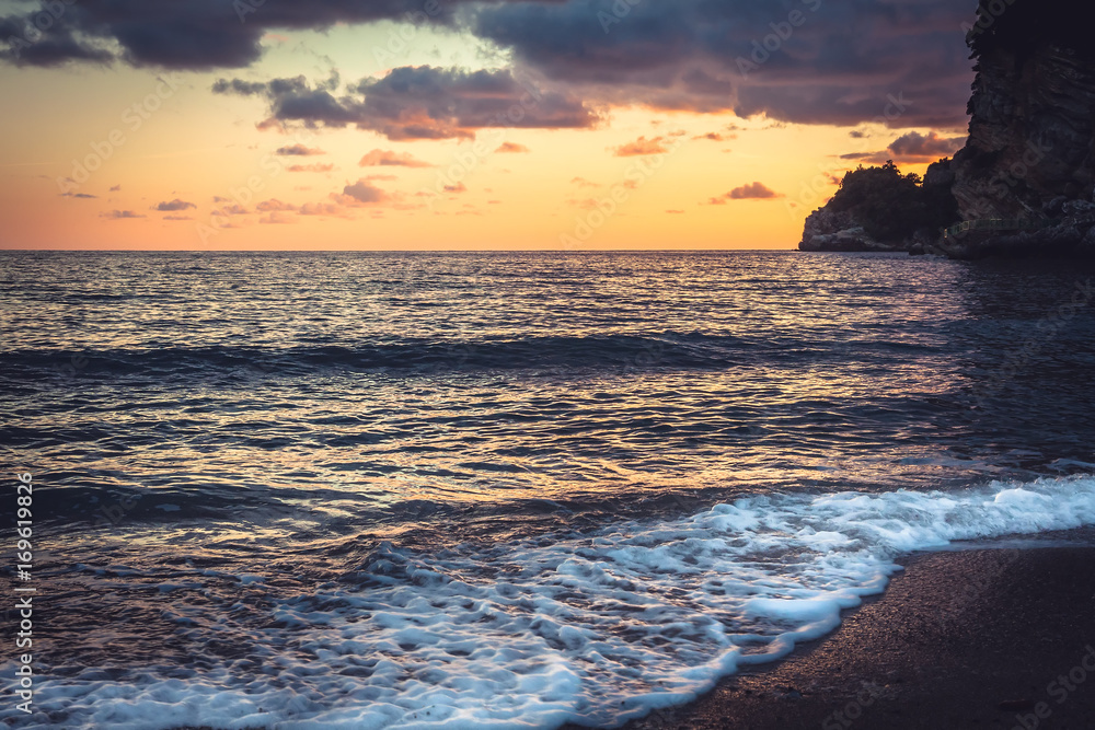 Obraz premium Surf at sunset beach with vibrant dramatic orange sky and cliffs on Montenegro coastline