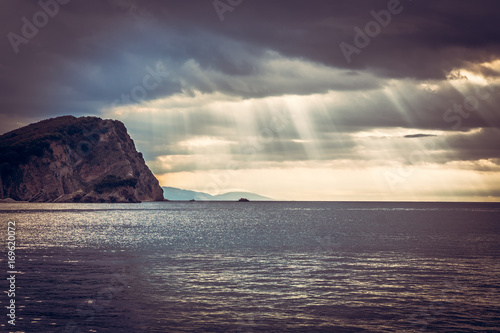 Scenic landscape with cliff rock at sea during sunset with sun rays breaking through dramatic clouds  during sunset and copy space © splendens