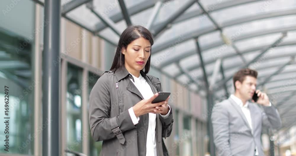 Businesswoman waiting for train on platform with smartphone in hand Businesswoman waiting for train on platform with smartphone in hand