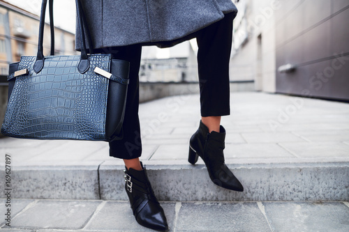 Elegant outfit. Close up of textured big dark blue bag. Model posing in street, wearing short trousers, black pointed toe ankle boots. Female fashion concept. Copy, empty space for text