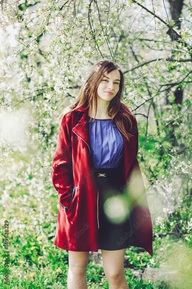 Beautiful brown-eyed girl in a red coat standing among trees Beautiful brown-eyed girl in a red coat standing among trees