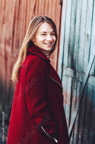 smiling girl with dental braces. woman is wearing in red coat and standing near the wooden door