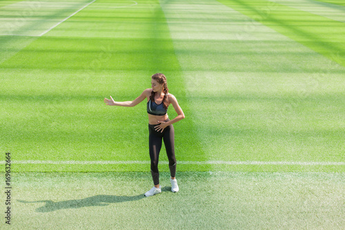 Fitness sporty girl in fashion sportswear and hip-hop dance at a football stadium, outdoor sports. Happy sexy woman having fun on the background of green grass