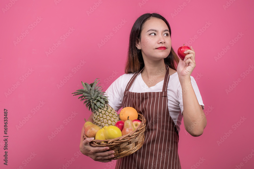 Portrait of happy young woman asian holding fruits basket while standing at studio.