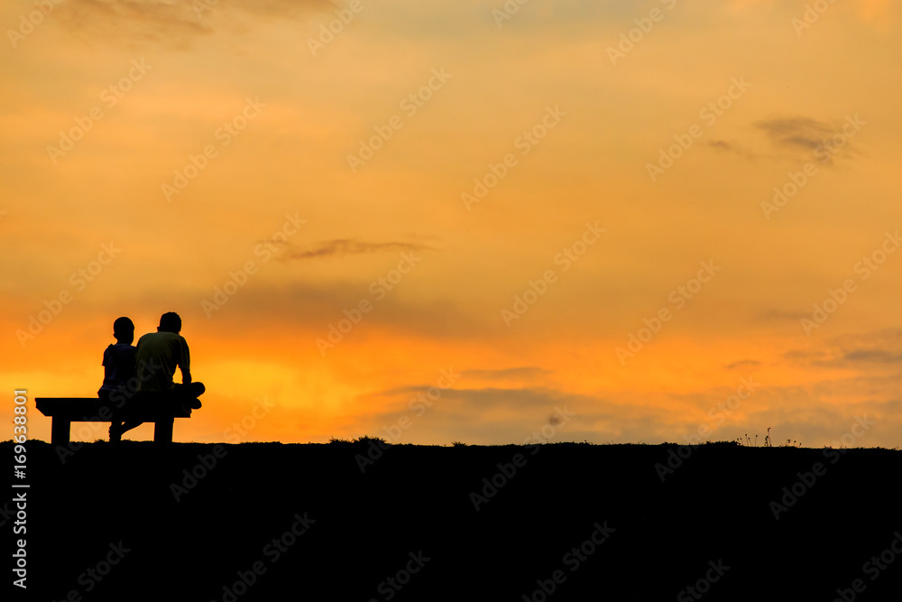 son and dad sitting on Chair at colorful sunset on background
