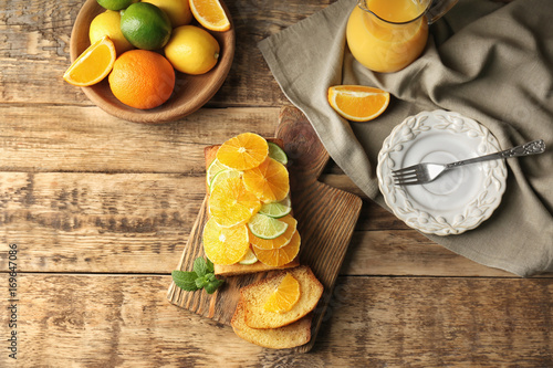 Cutting board with delicious sliced citrus cake and fruits on wooden table
