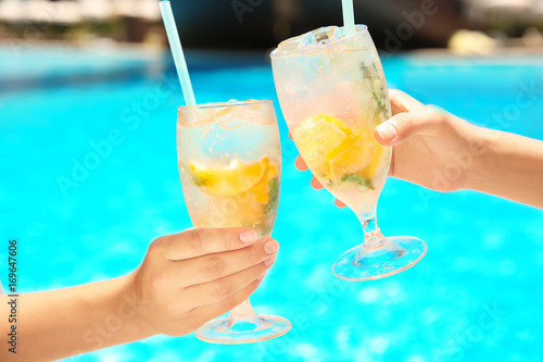 Young women with glasses of lemonade near swimming pool