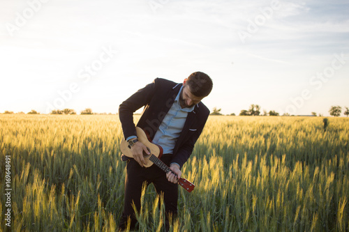 Happy manager with ukulele travel in summer wheat fields, buisinesman in suit play on ukulele, vacation or travel concept photo 