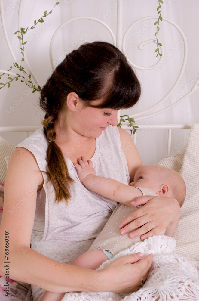Breastfeeding baby. Young mother holding her newborn child. Mom nursing baby. Woman and new born boy in white bedroom.