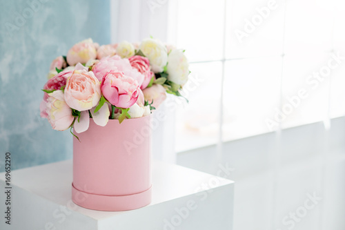 Flowers in round luxury present box. Bouquet of pink and white peonies in paper box near the window.Mock-up of hat box of flowers with free copyspace for text. Interior decoration in in pastel colors.