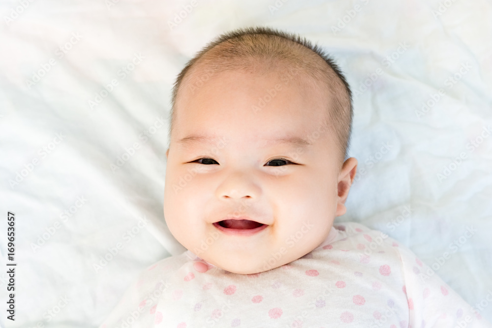 Portrait of adorable baby girl lying on back on the bed and looking in camera indoors Portrait of adorable baby girl lying on back on the bed and looking in camera indoors