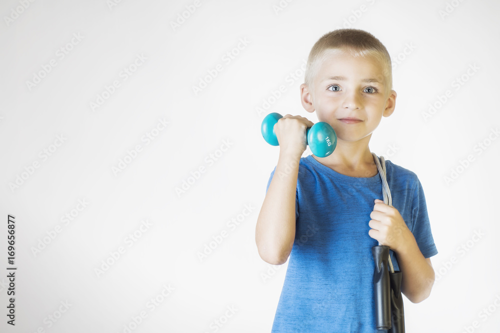 Boy with skipping rope and dumbbell. Portrait happy, smiling boy holding a jump rope and dumbbell. Looking at camera. The concept of a healthy lifestyle, sport or workout. Boy with skipping rope and dumbbell. Portrait happy, smiling boy holding a jump rope and dumbbell. Looking at camera. The concept of a healthy lifestyle, sport or workout.