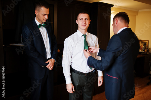 Groomsmen helping groom to dress up and get ready for his wedding ceremony.