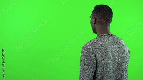 A young black man with his back to the camera waits for someone - green screen studio