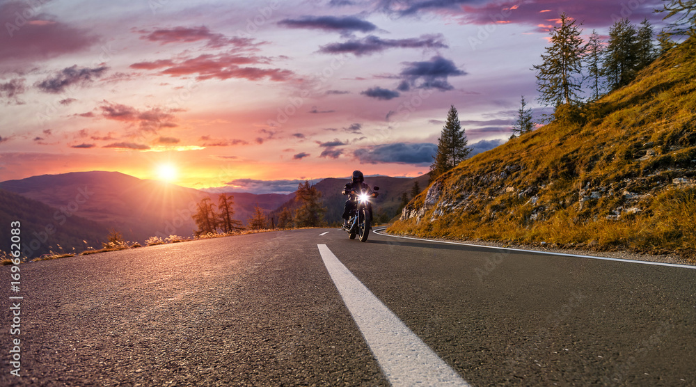 Naklejka premium Kierowca motocykla jedzie na autostradzie alpejskiej. Fotografia plenerowa, krajobraz górski.