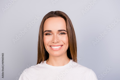 Close up portrait of successful young brown haired lady entrepreneur in white casual t shirt, standing on the pure light grey background, with beaming smile